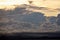 The clouds are multicolored, thunderous bizarre shapes against the blue sky and the sun above the ocean surface.