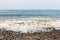 Cloudy day on the beach side with waves hitting seashore. Sea foam on the waves. Rocky beach with colorful stones. Blue sky withou