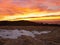 A cloudy daybreak above inversion and hills. Dark peaks of trees make contrast with yellow and orange clouds on the sky, last snow