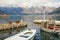 Cloudy Mediterranean landscape with snow-capped mountains and fishing boats in small harbor. Montenegro, Bay of Kotor