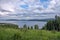 Cloudy sammer landscape of the lake with a blooming hill and mountains in the distance.