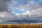 Cloudy sky before a thunderstorm, a field with a road going into the distance. Residential buildings near the horizon