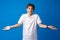 Clueless and confused teen boy with raised arms on blue background