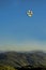 Cluster of balloons flying over a mountain top.