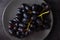 A cluster of juicy black grapes lies in a gray plate on a dark gray table