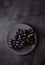 A cluster of juicy black grapes lies in a gray plate on a dark gray table. Photo dark and mood