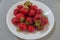 Clusters of ripe strawberries lying on top of each other in a white ceramic plate, standing on a grayish-silver tablecloth