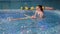 A coach teaches a little girl to swim on her back in an indoor pool.