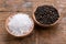 Coarse crystal salt and whole black peppercorns in small wooden bowls