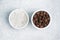 Coarse salt and black peppercorns in white ceramic bowls on gray concrete background, copy space top view