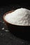 Coarse white salt in a wooden bowl on the black background