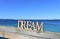 Coast with Dream wooden sign on a handrail. Blue sea, sunny day. Rias Baixas, Spain.