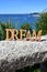 Coast with Dream wooden sign on a handrail and trees. Blue sea, sunny day. Rias Baixas, Spain.