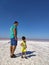 The coast of the salty Pink Lake in the Crimea. A man in blue breeches and a little boy in yellow clothes with a bottle of water.