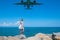 Coastal Encounter: Girl in White Dress on Stones, Plane Beckoning from the Blue Sea