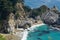 Coastal waterfall cascading onto Pacific white sand beach surrounded by rocky cliffs