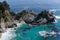 Coastal waterfall cascading onto Pacific white sand beach surrounded by rocky cliffs