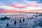 Coastal waterfront leading to distant port facility and cranes on horizon under intense sunset colored sky