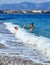 A coastal wave knocks down a young lady who enters the sea by a pebble beach