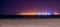 The coastline of Blankenberge beach lighted by night, colorful lights on the industry terrain in the distance