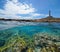 Coastline with a lighthouse and rocky seabed with fish underwater