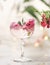 Cocktail in champagne glass with pink rose petal and green leaf at grey table with blurred background. Romantic fancy drink for