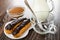 Cocoa powder in bowl, pitcher with hot milk, eclairs with chocolate in plate, spoon in cup on wooden table