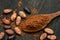 Cocoa powder on a wooden spoon isolated on black rustic wood board from above. Spilt cocoa and roasted peeled and unpeeled cocoa