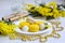 Coconut cookies and yellow macaroons on a white plate, branches of mimosa, craft rolls on a light wooden background