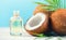 Coconut palm oil in a bottle with coconuts and green palm tree leaf on blue background. Coco nut closeup. Healthy food, skincare