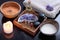 A coconut shell with milk alongside a spa treatment set with orange bath salt, purple massage salt, hot stones, aromatic