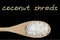 Coconut shreds on wooden spoon isolated on black background