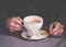 Coffe cup in hands of a man against dark sweater background. Hot latte in beautiful white cup with biscuit. Morning in cafe