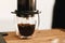 Coffee in aeropress, alternative coffee brewing method. Aeropress and glass cup, spoon on wooden table, coffee drops closeup in