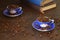 Coffee bean in the blue cups and vintage book stacking on wooden table in morning light