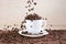 Coffee beans falling down into white cup standing on white plate standing on tablemat.