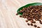 Coffee beans on a green leaf and scattered on a light wooden table, closeup grains, place to insert text, copy space