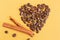 Coffee beans laid out in the shape of a heart with cinnamon sticks on a yellow background. Love for coffee.