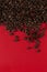 Coffee beans are scattered on a red paper background close-up, commercial copy space