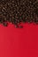 Coffee beans are scattered on a red paper background close-up, commercial copy space