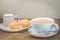 Coffee break. Muffins and blue mug with cappuccino and cream in a small cup for breakfast on a wooden table. Background with copy