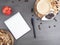 Coffee break in the workplace. White cup of coffee, apple, dates, mix of nuts in wooden bowl, notepad, pen on grey