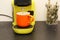 Coffee in a bright orange Ñup on the table. Close-up is a light green coffee maker with an orange cup