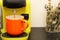 Coffee in a bright orange Ñup on the table. Close-up is a light green coffee maker with an orange cup