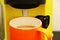 Coffee in a bright orange Ñup on the table. Close-up is a light green coffee maker with an orange cup