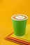 Coffee Cappuccino in a paper green cup on colorful yellow background. Mockup. Cappuccino coffee take away. Space for