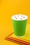 Coffee Cappuccino in a paper green cup on colorful yellow background. Mockup. Cappuccino coffee take away. Space for