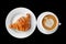Coffee and croissant breakfast on a plain black background.