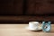 Coffee cup and clock on wooden table against defocused sofa with pillows. Front view. Good morning concept. Mock-up