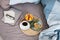 Coffee cup, cold tartlets and grapefruit on wooden tray, laptop, eyeglass and notebook on bedding. Breakfast in bed, cosy morning